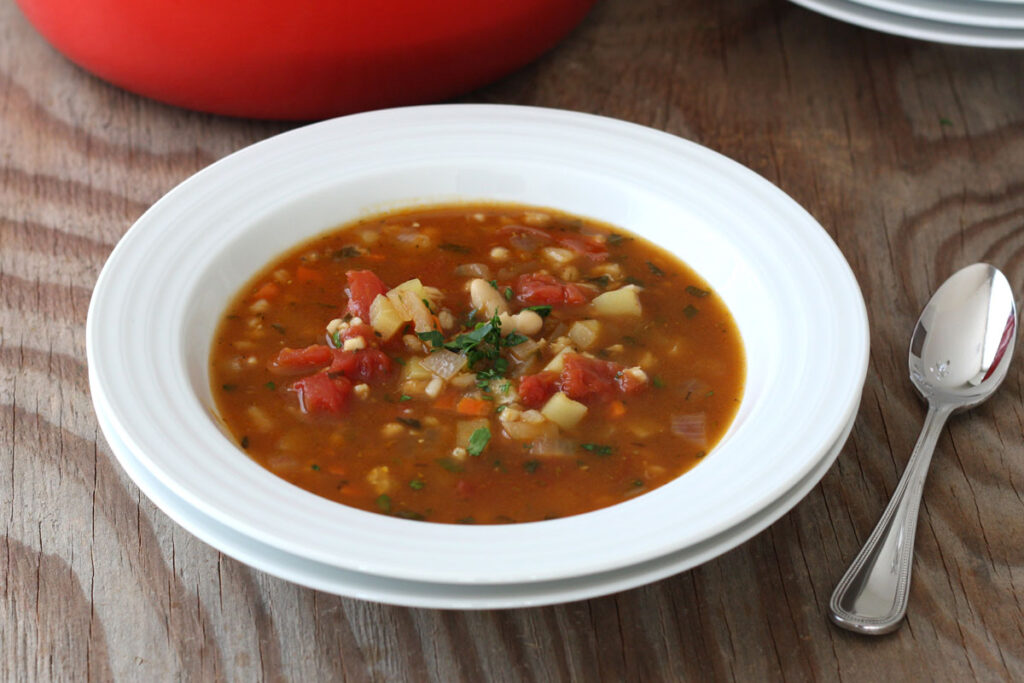 Vegetable barley soup in white plate with spoon.