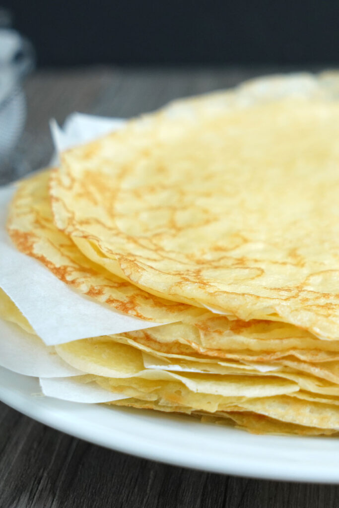 Stack of finished cooked crepes with parchment between each crepe.