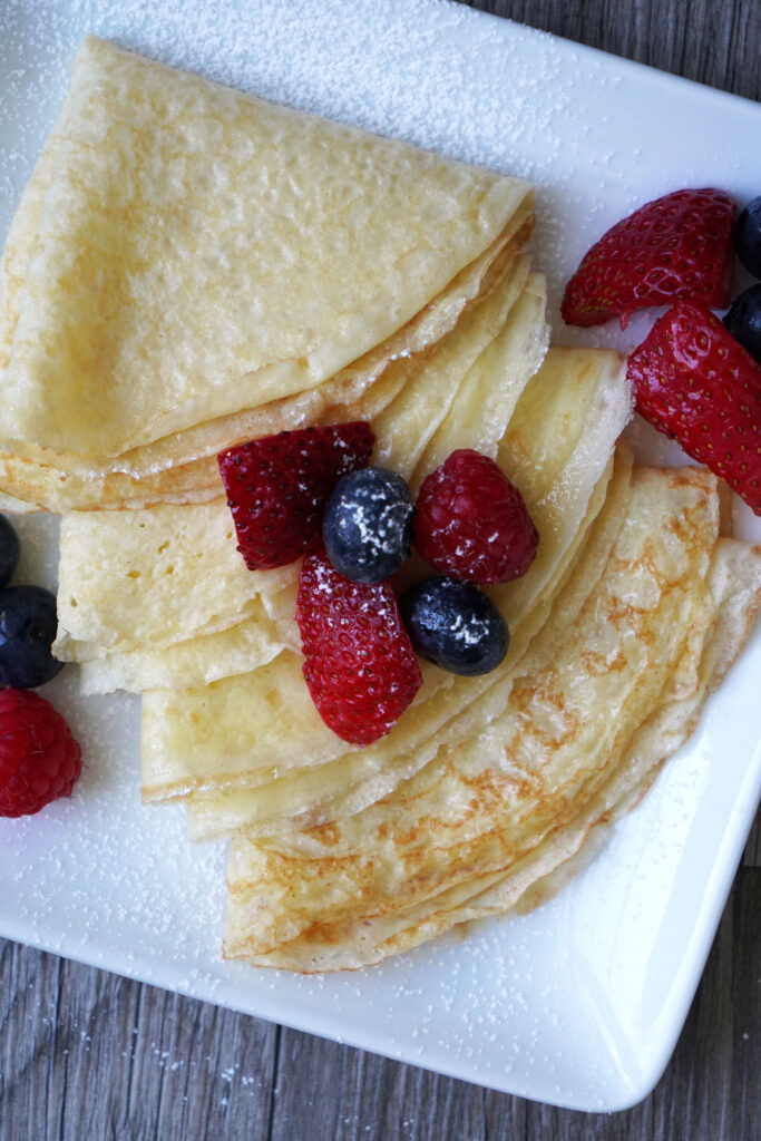 Close up of crepes, folded into triangles, served with fresh fruit.