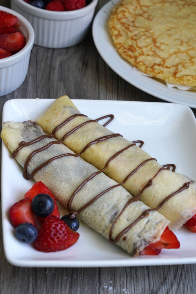 Rolled crepes stuffed with Nutella and strawberries on a white plate.