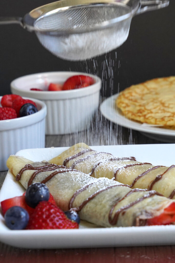 Powdered sugar being sprinkled on Strawberry Nutella rolled crepes.