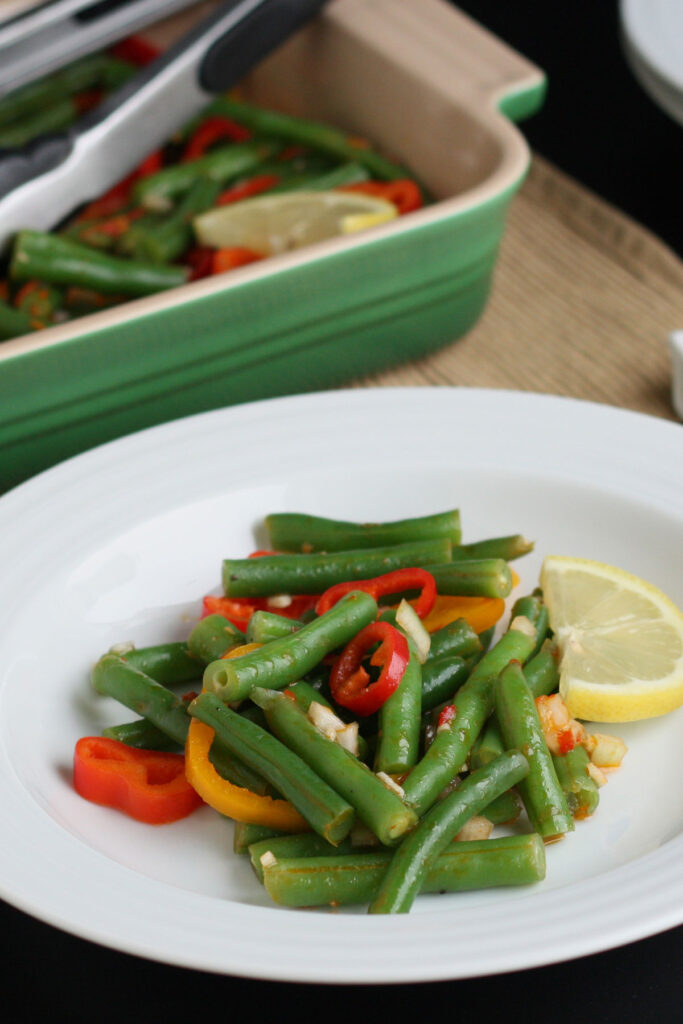 Serving of green bean salad with lemon harissa dressing on a white plate.