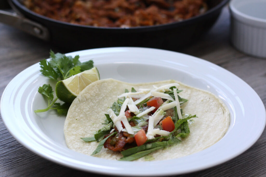 Open seitan taco showing filling ingredients: setian, spinach, tomato, cheese.