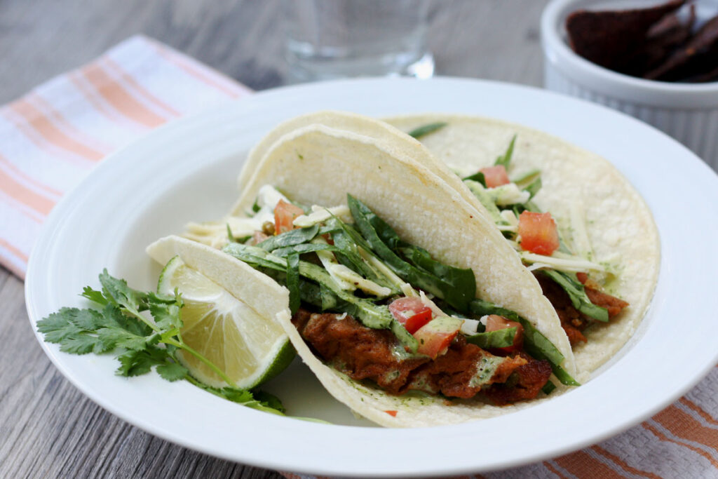 Seitan tacos in white plate with lime garnish.