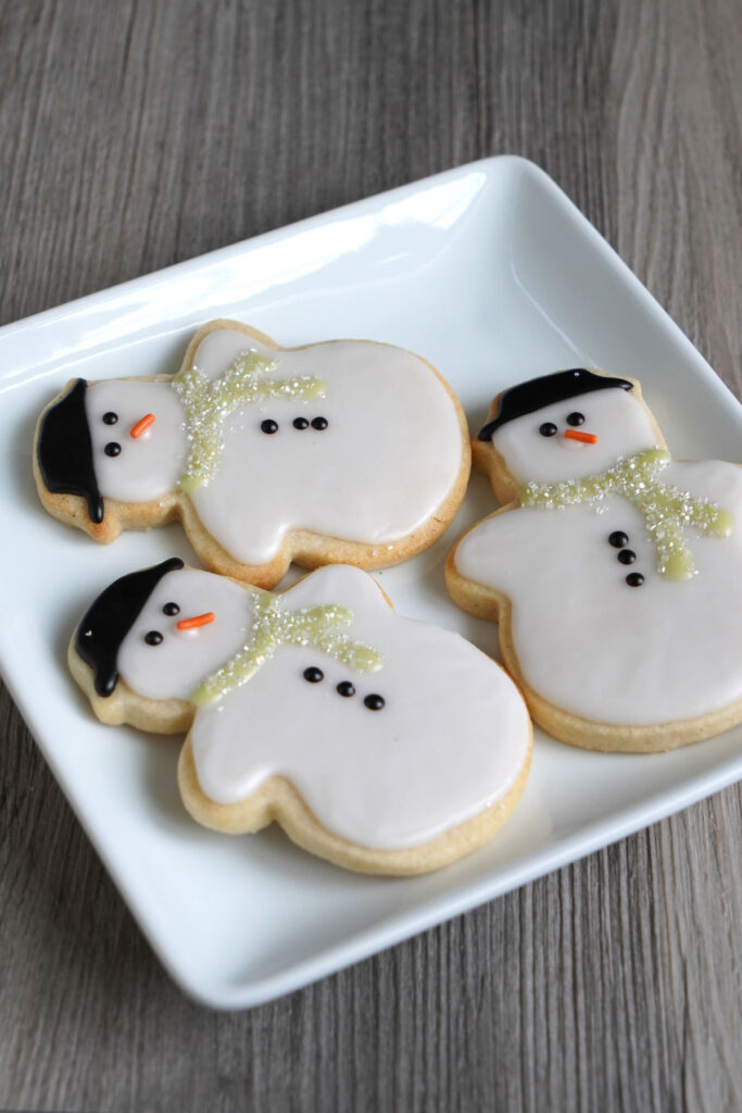 Three snowman cookies on a white square plate.