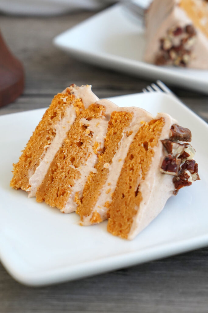 Close up view of a slice of sweet potato cake with cinnamon frosting and candied pecans.