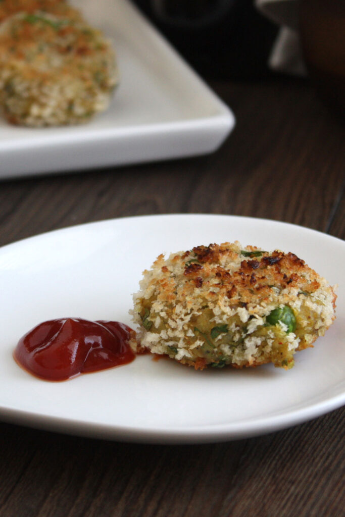 Aloo tikki in a white plate served with ketchup.