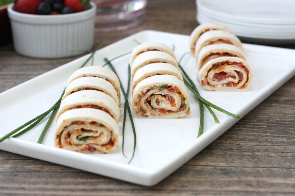 Tortilla rollups sliced on a white plate with chives garnish. 