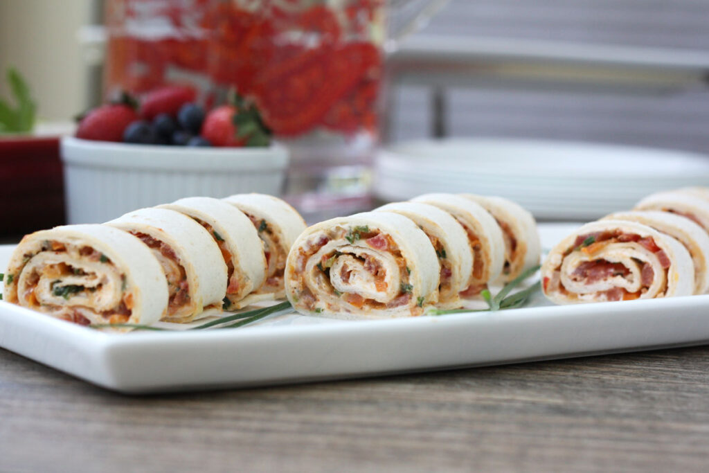 Tortilla rollups sliced on a white plate with chives garnish. 