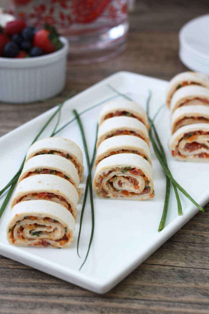 Tortilla rollups sliced on a white plate with chives garnish. 