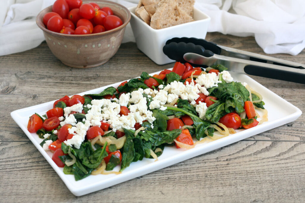 Platter of spinach salad with bread and more cherry tomatoes in the back ground.