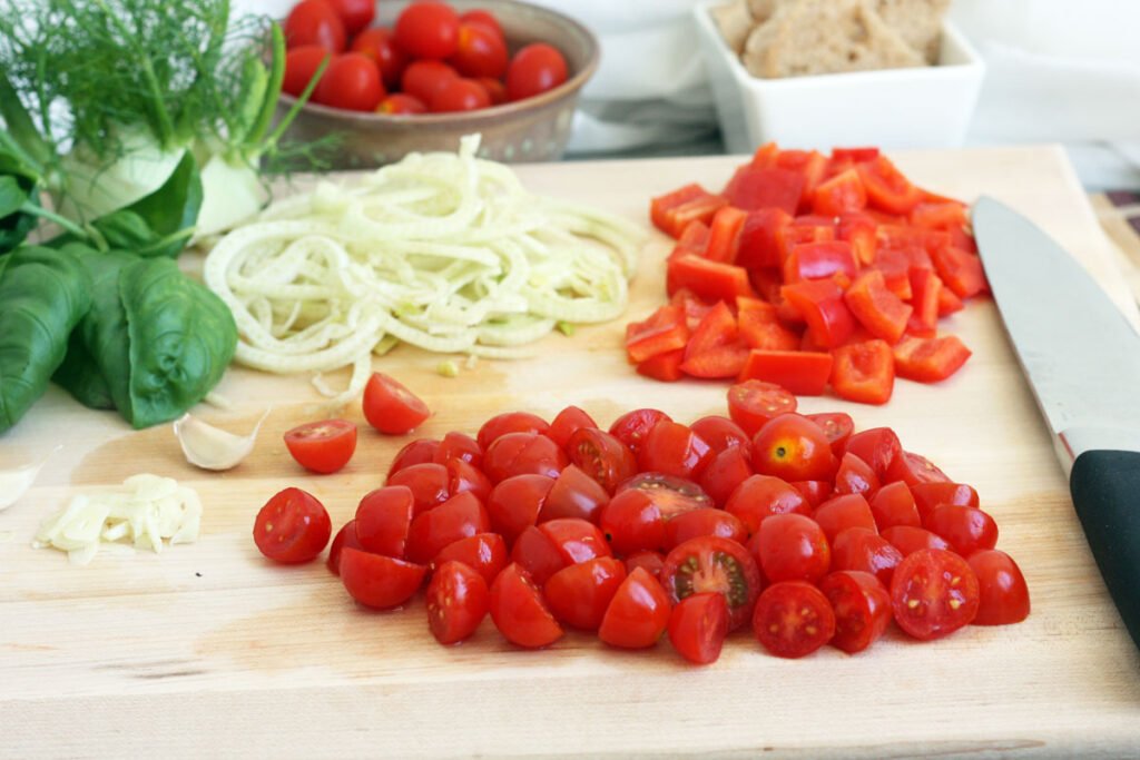 Chopped tomatoes, fennel and bell pepper on a cutting board.