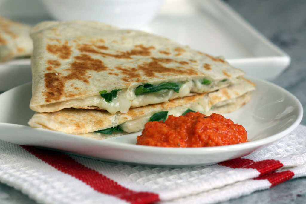 Two white bean quesadillas with roasted red pepper sauce in a white plate on a napkin.