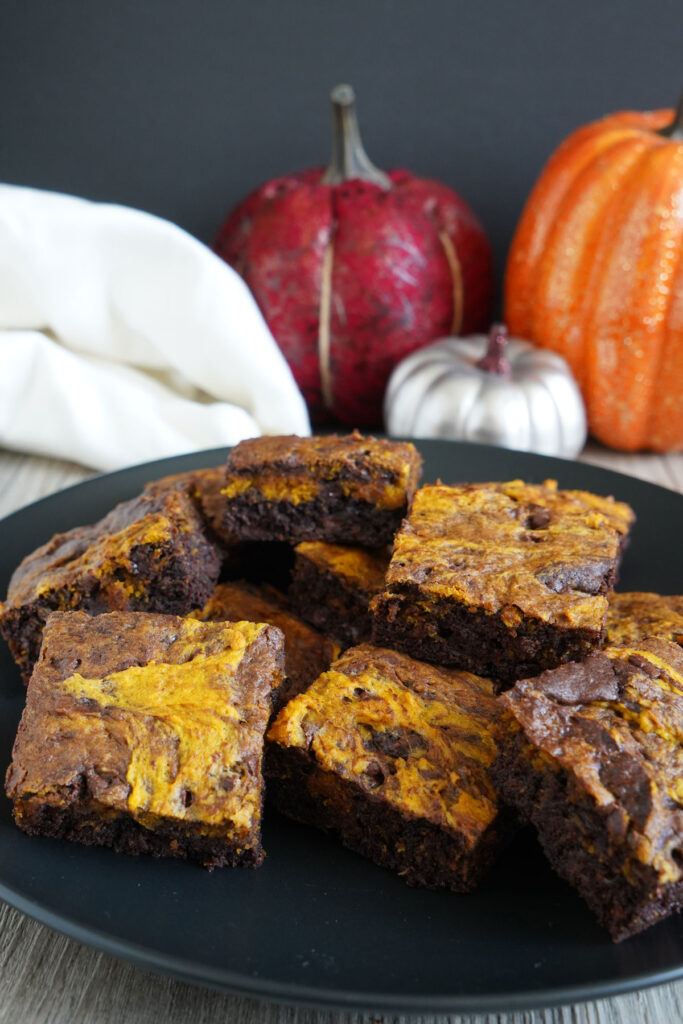 Pumpkin brownies on a black plate with decorative pumpkins in background.