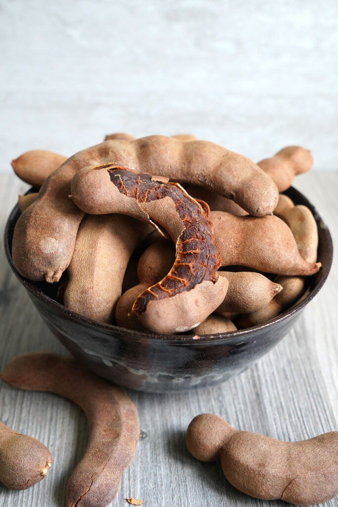 Tamarind pods in a bowl with one pod having the shell peeled open.