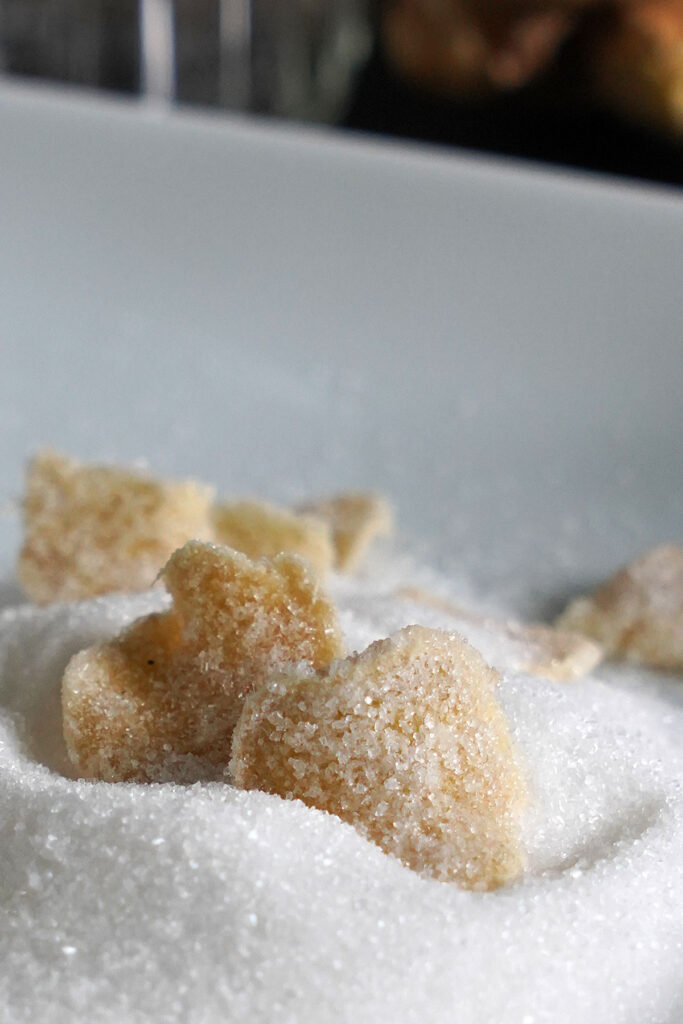 Candied ginger slices being coated in sugar.