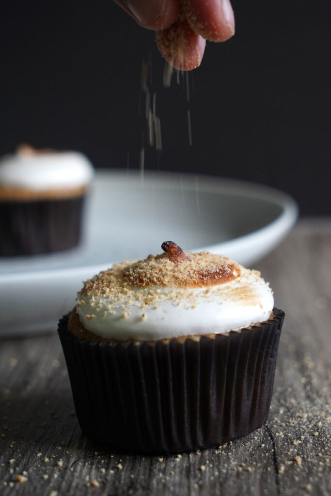 Graham cracker crumbs being sprinkled on top of finished cupcake.