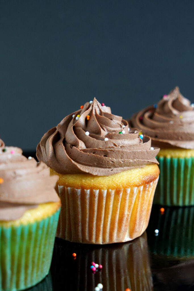 Three frosted vanilla cupcakes in a row.