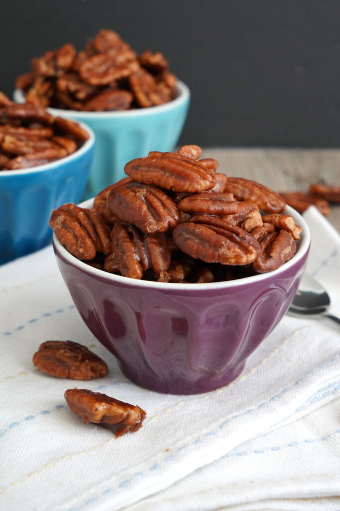 Candied pecans in small purple bowl on top of napkin.