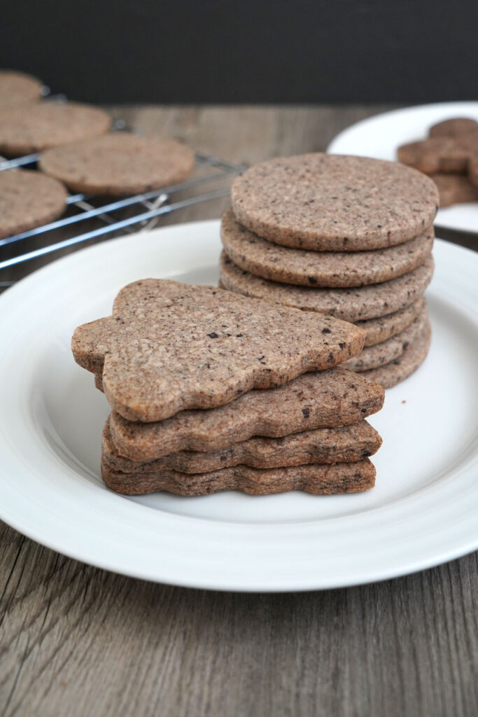 Stacks of tree shaped cookies and circles shaped cookies on a white plate. 