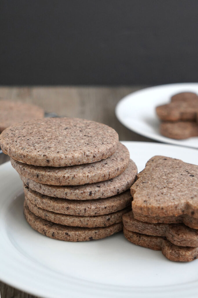 Stacks of tree shaped cookies and circles shaped cookies on a white plate.