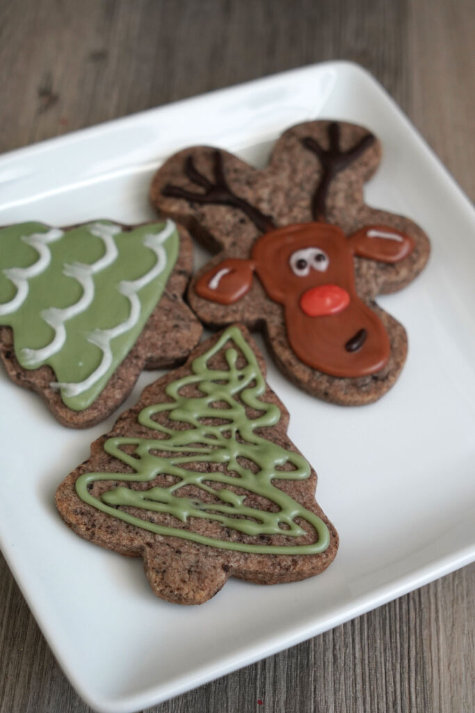 Decorated tree and reindeer cookies on a white plate.