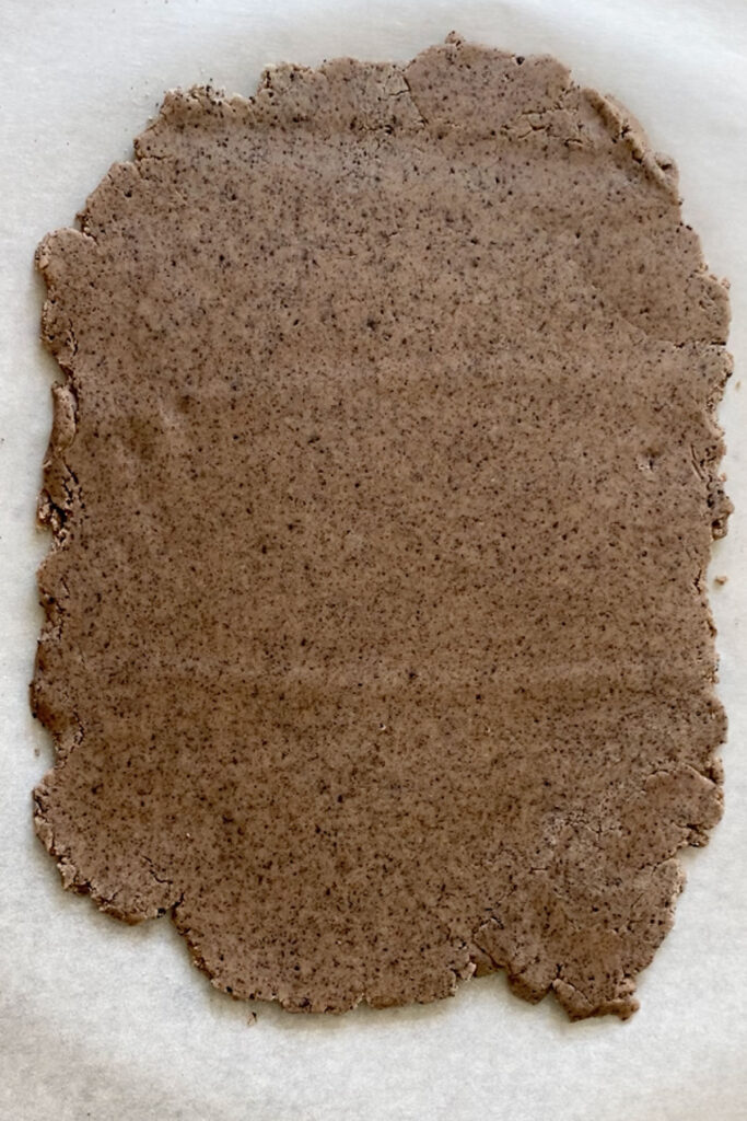 Cookies and cream sugar cookie dough rolled out on parchment paper.