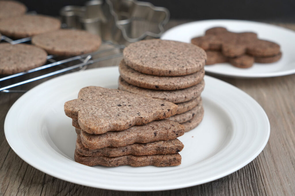 Stacks of tree shaped cookies and circles shaped cookies on a white plate. 