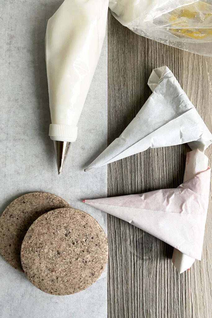 Unfrosted cookies with piping bag filled with white icing and parchment cones filled with colored icing.