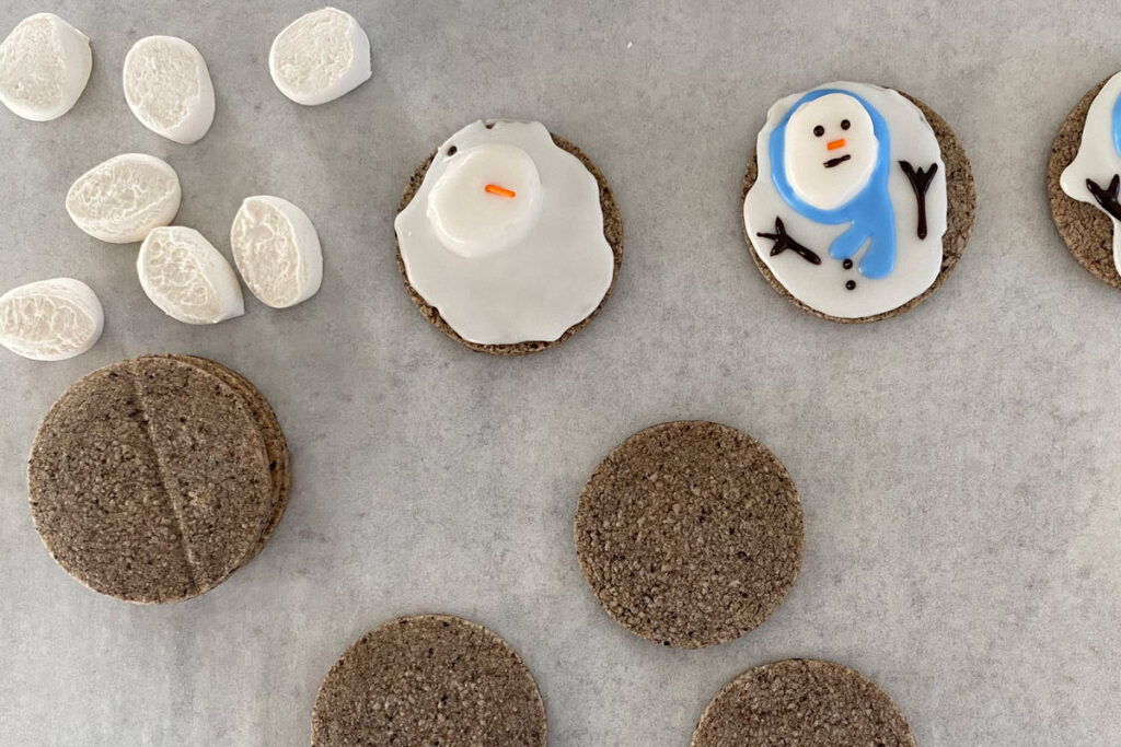 Parchment paper with cookies, marshmallows, half iced cookie, completely iced cookie.