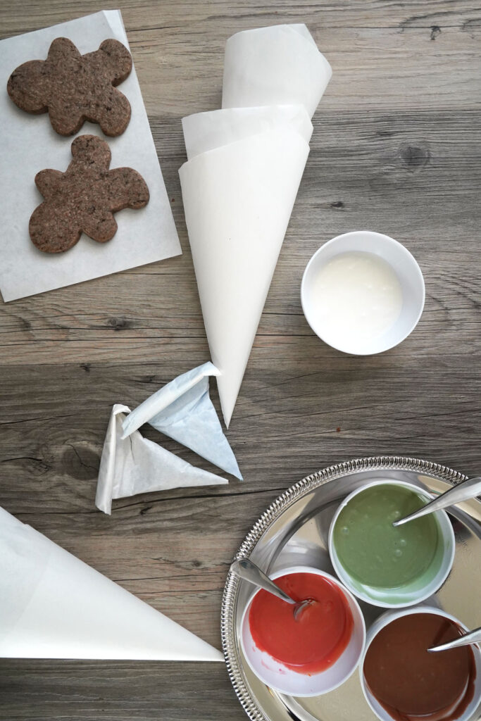 Top view of parchment cones, undecorated cookies, icing colors. 