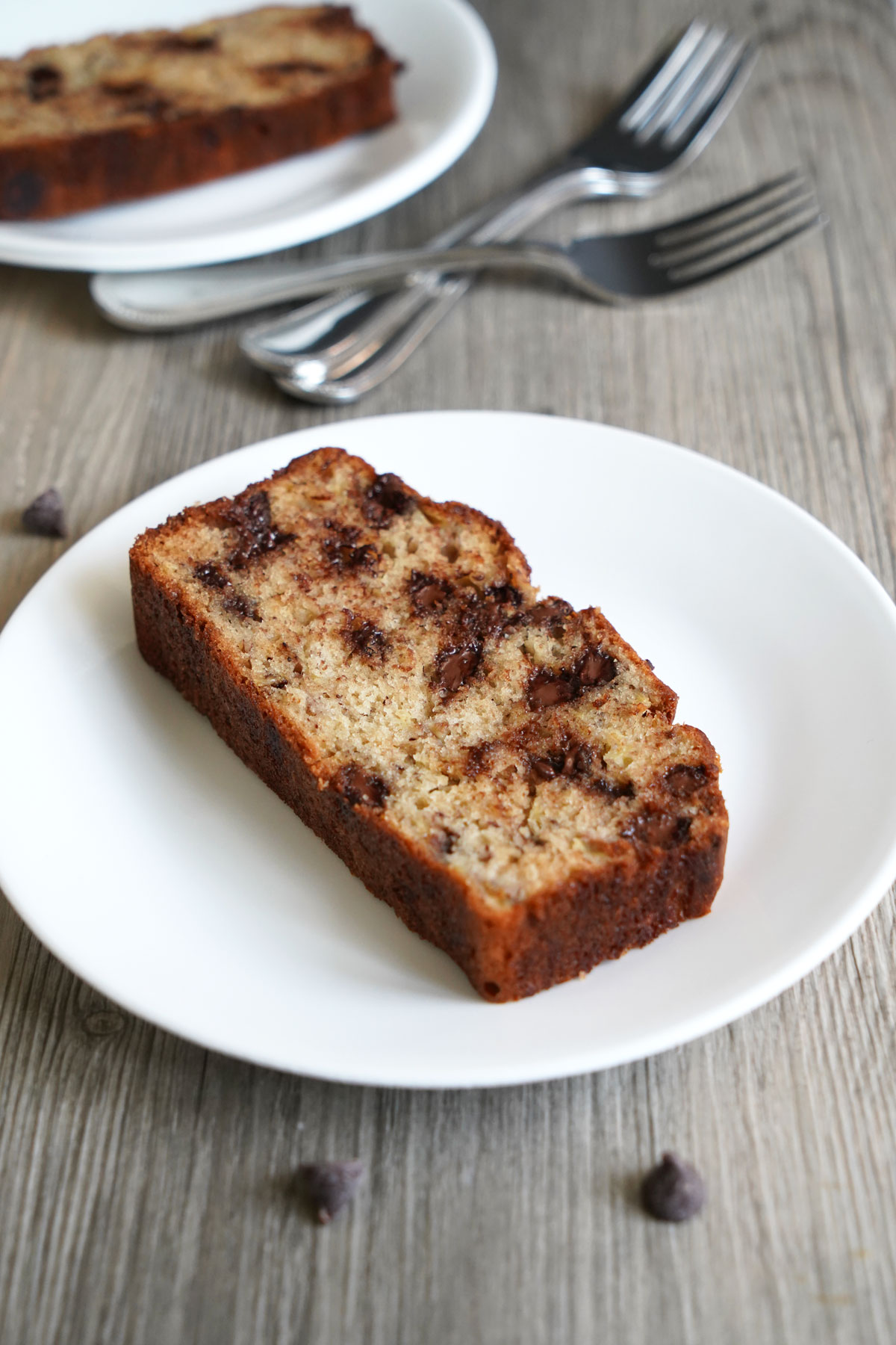 Slices of chocolate chip banana bread on plates next to forks.