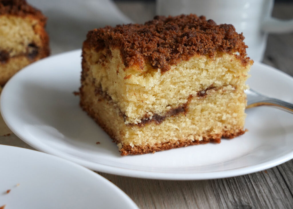 Slice of coffee cake on white plate with fork. 