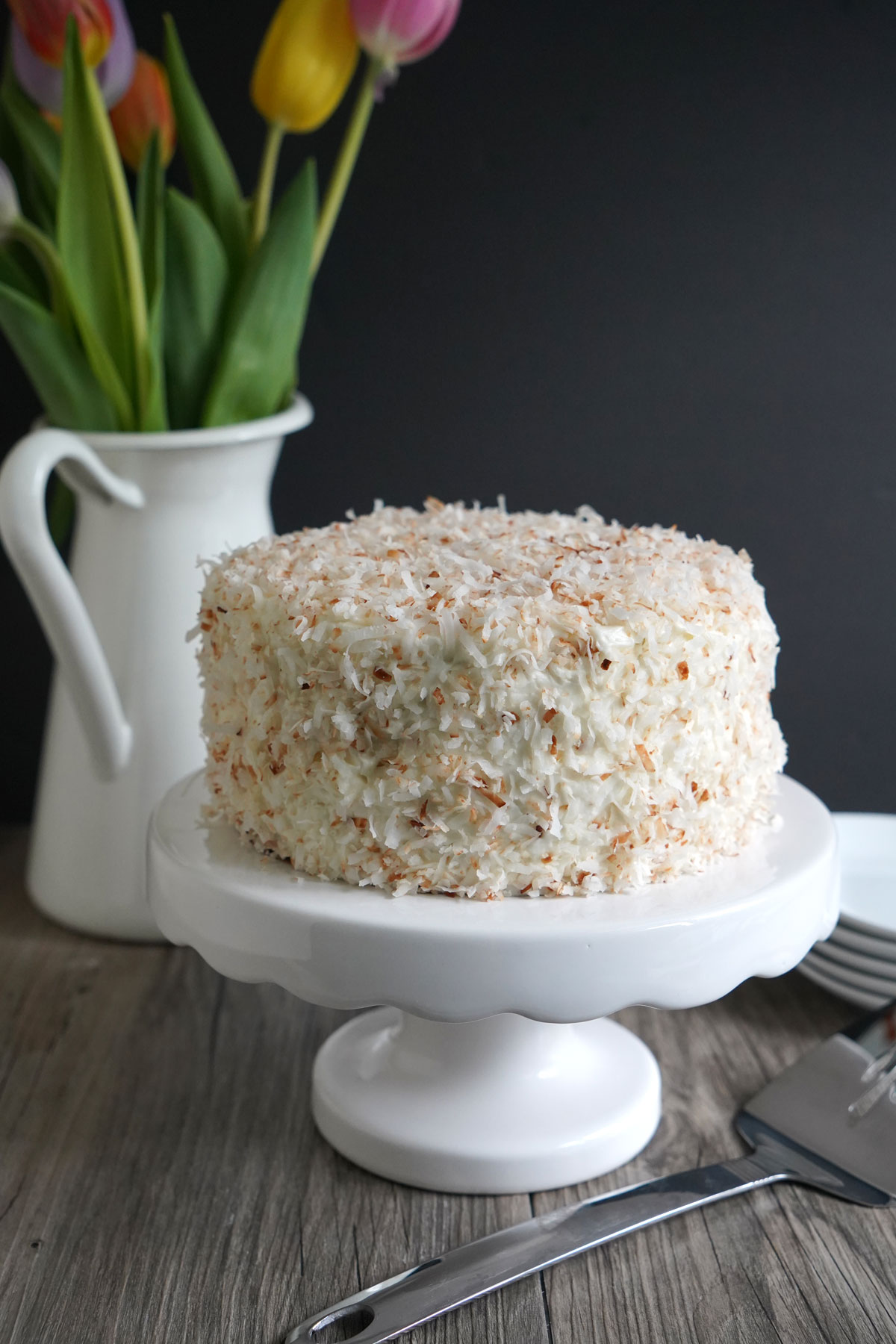 Uncut lemon coconut cake on white pedestal.