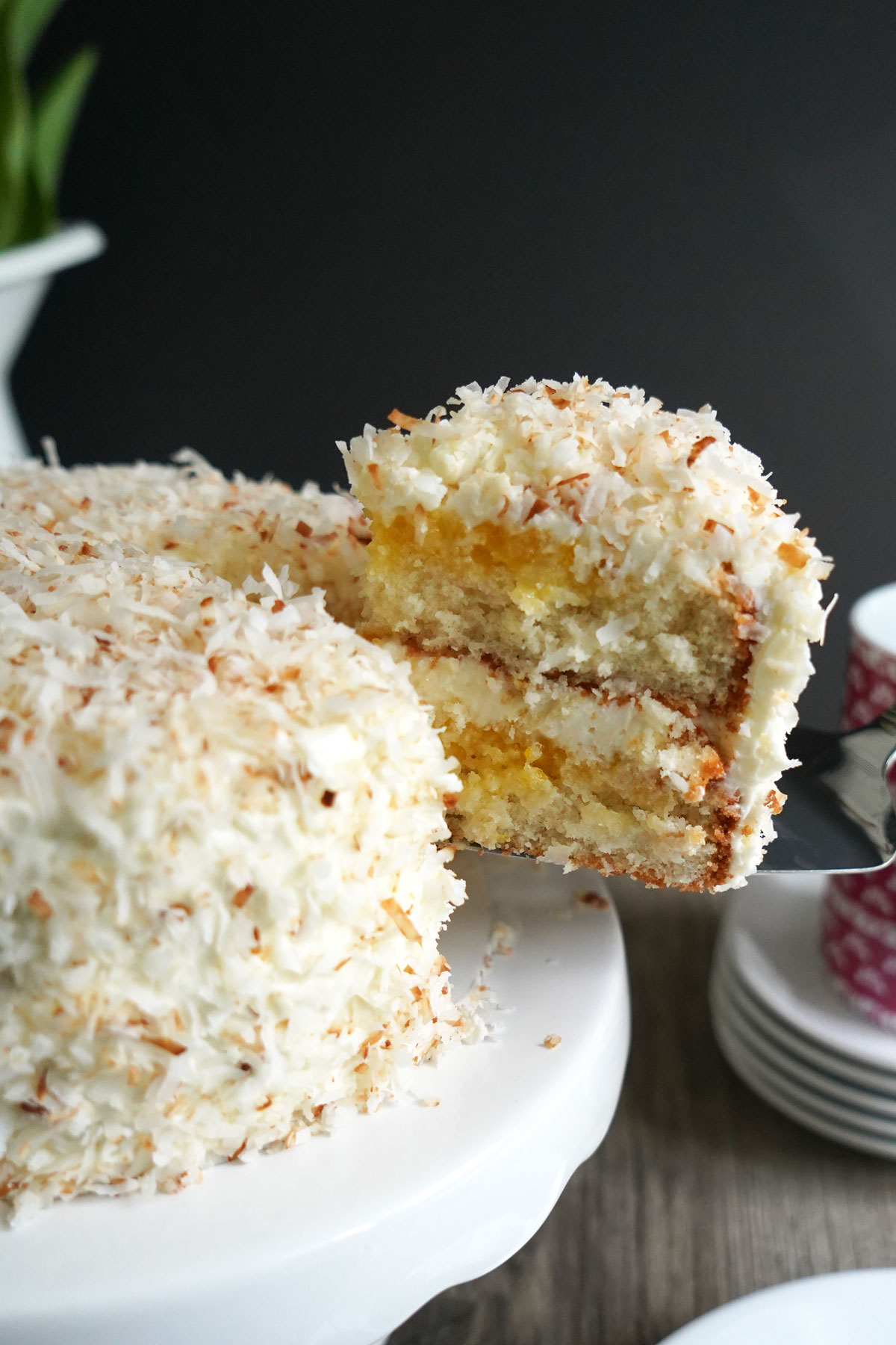 Cake slice being removed from lemon coconut cake on white pedestal.