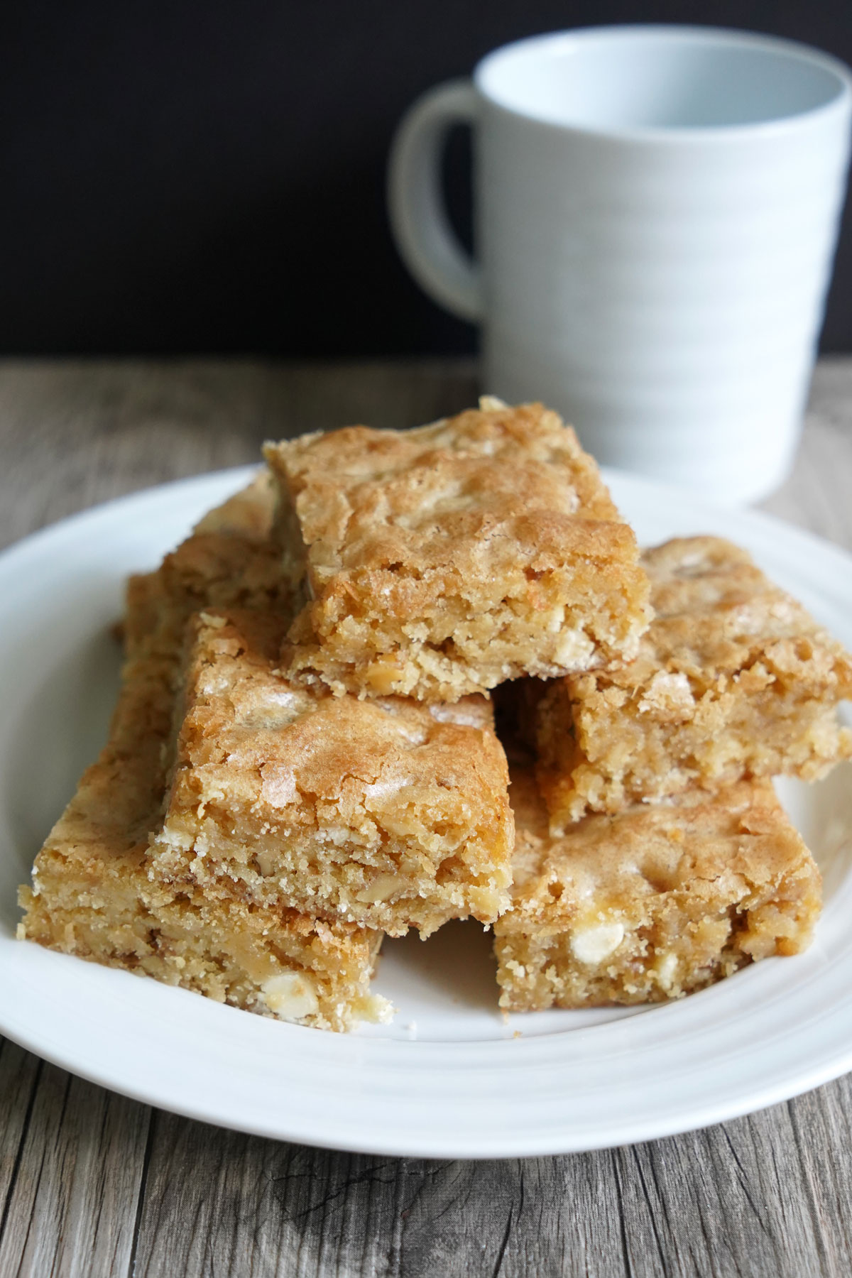 White Chocolate Blondie Bars on a white plate with mug in background.