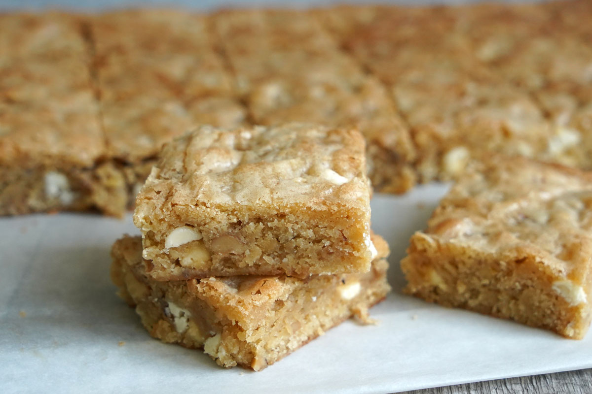 Two white chocolate blondies stacked with more in background.