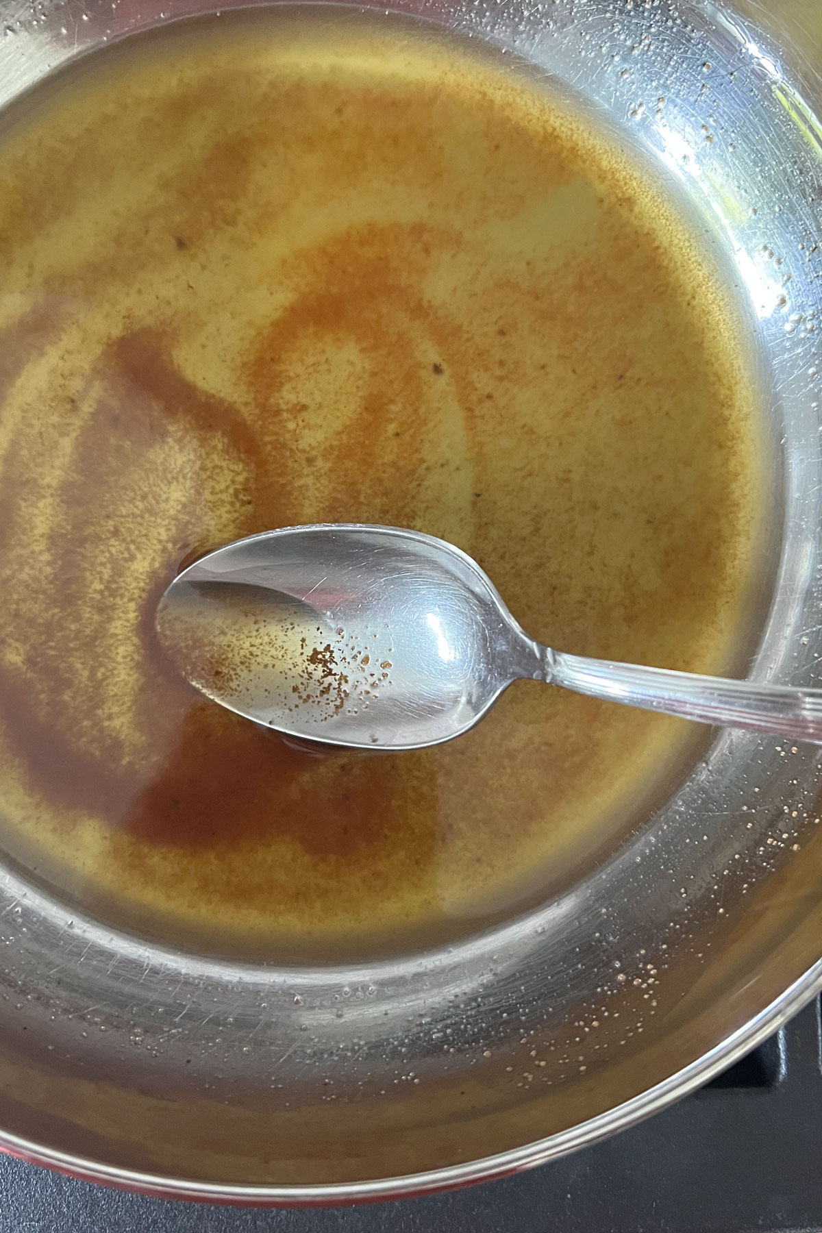 Browned butter in a stainless steel pan with spoon showing bits of browned milk solids.