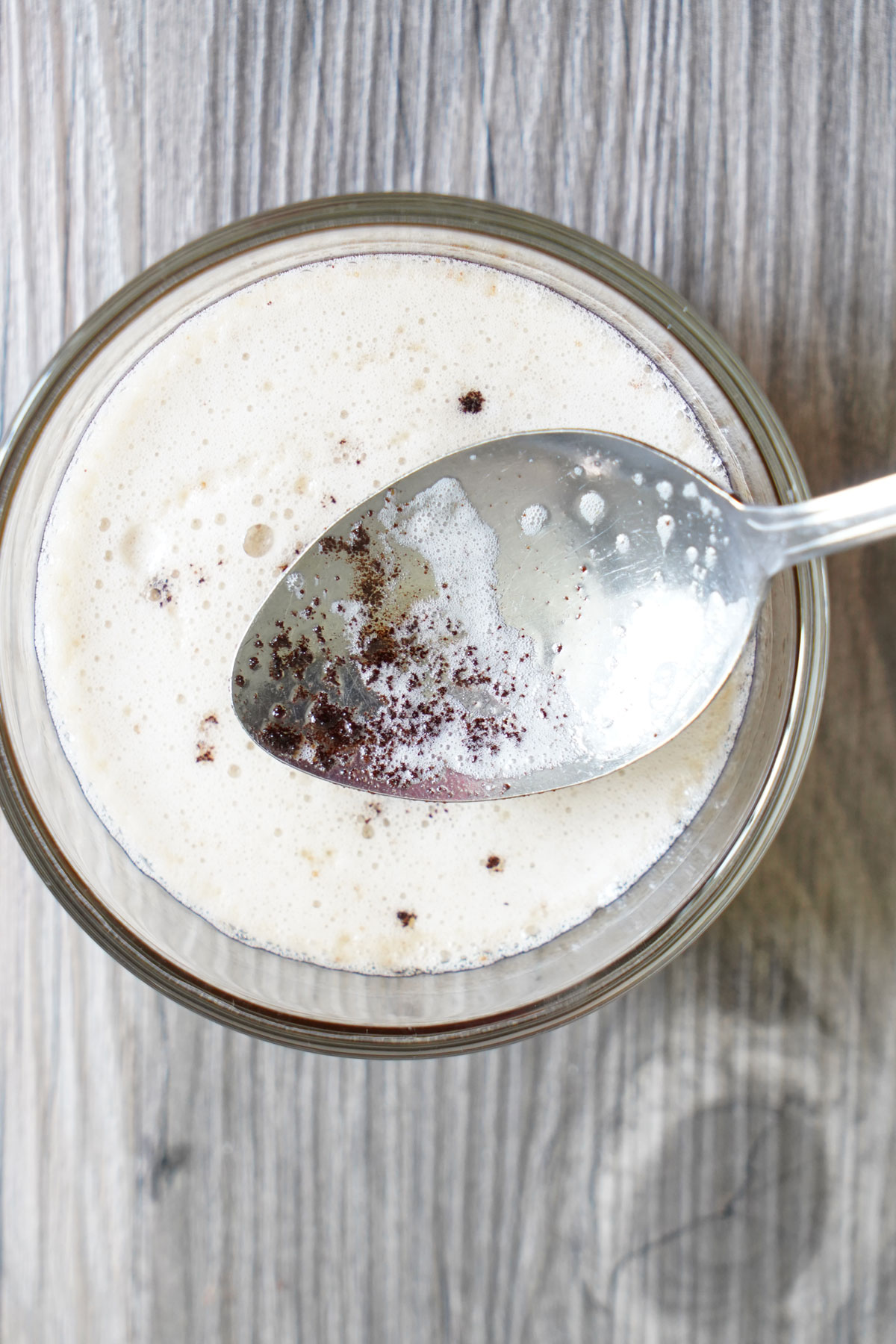 Brown bits of milk solids in a spoon held over container of browned butter.