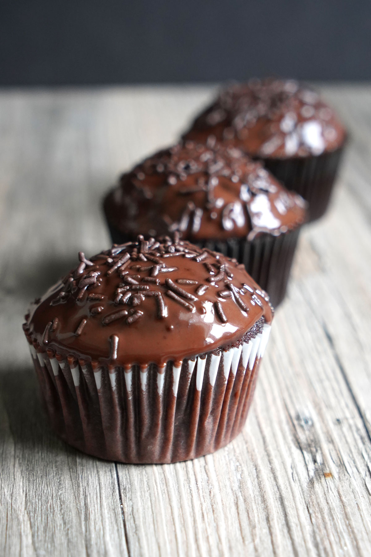 Three chocolate ganache cupcakes lined up in row.