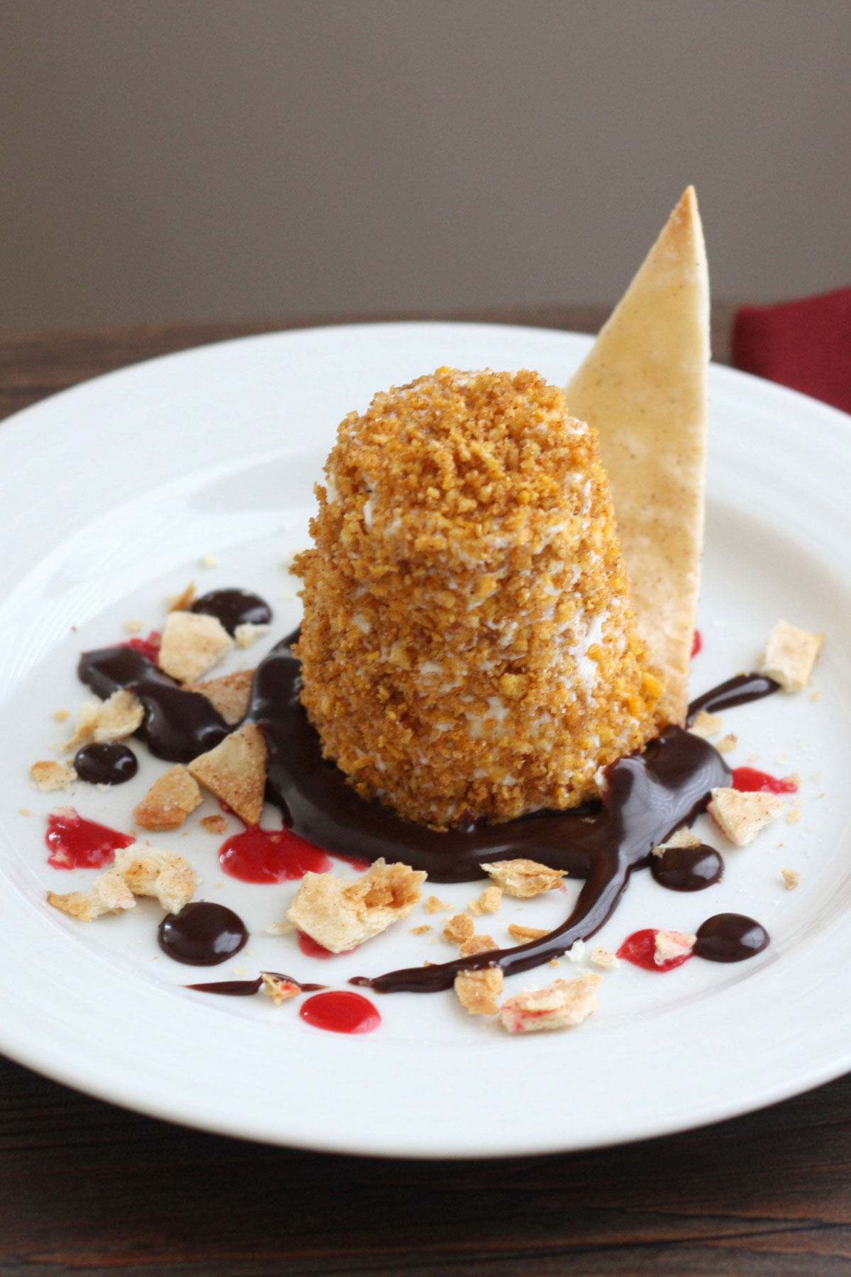 Mexican Fried Ice Cream in a plate surrounded by drops of chocolate sauce, raspberry sauce and crushed sweet tortillas.