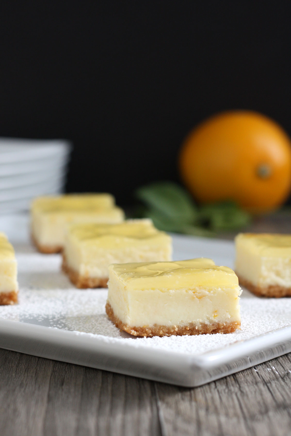 Meyer lemon cheesecake bars in a white plate with lemons in background.