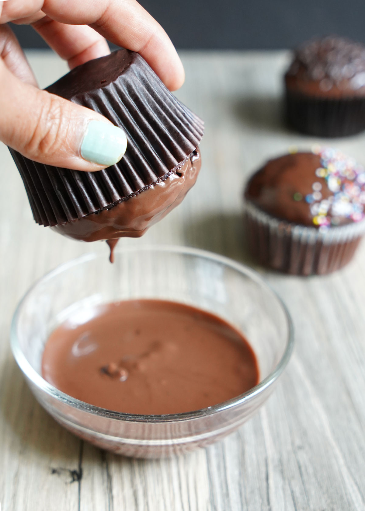 Cupcake being dipped in bowl of ganache.