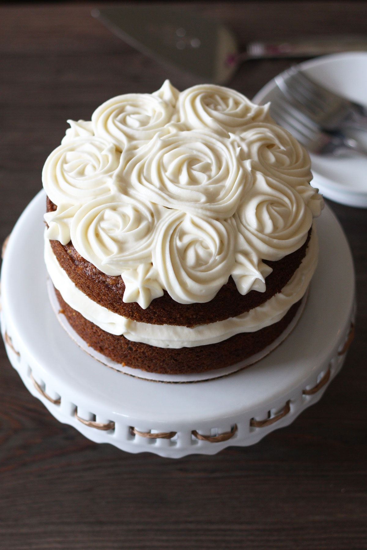 Carrot cake with cream cheese frosting flowers on top. Place on white cake stand. Top view.