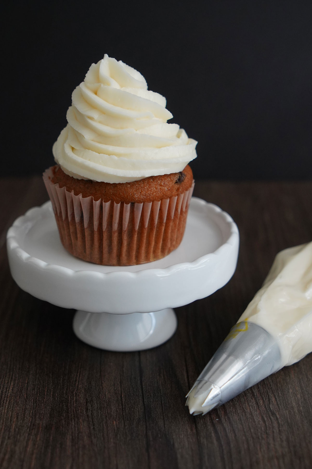 Cream cheese frosting on a cupcake with frosting piping bag to the side.