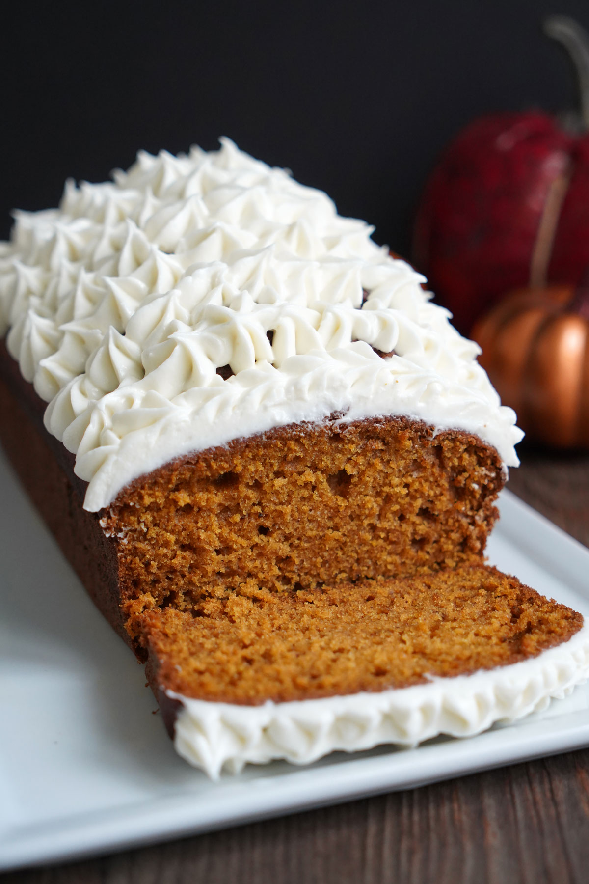 Pumpkin Bread loaf with cream cheese frosting on white plate with one slice.