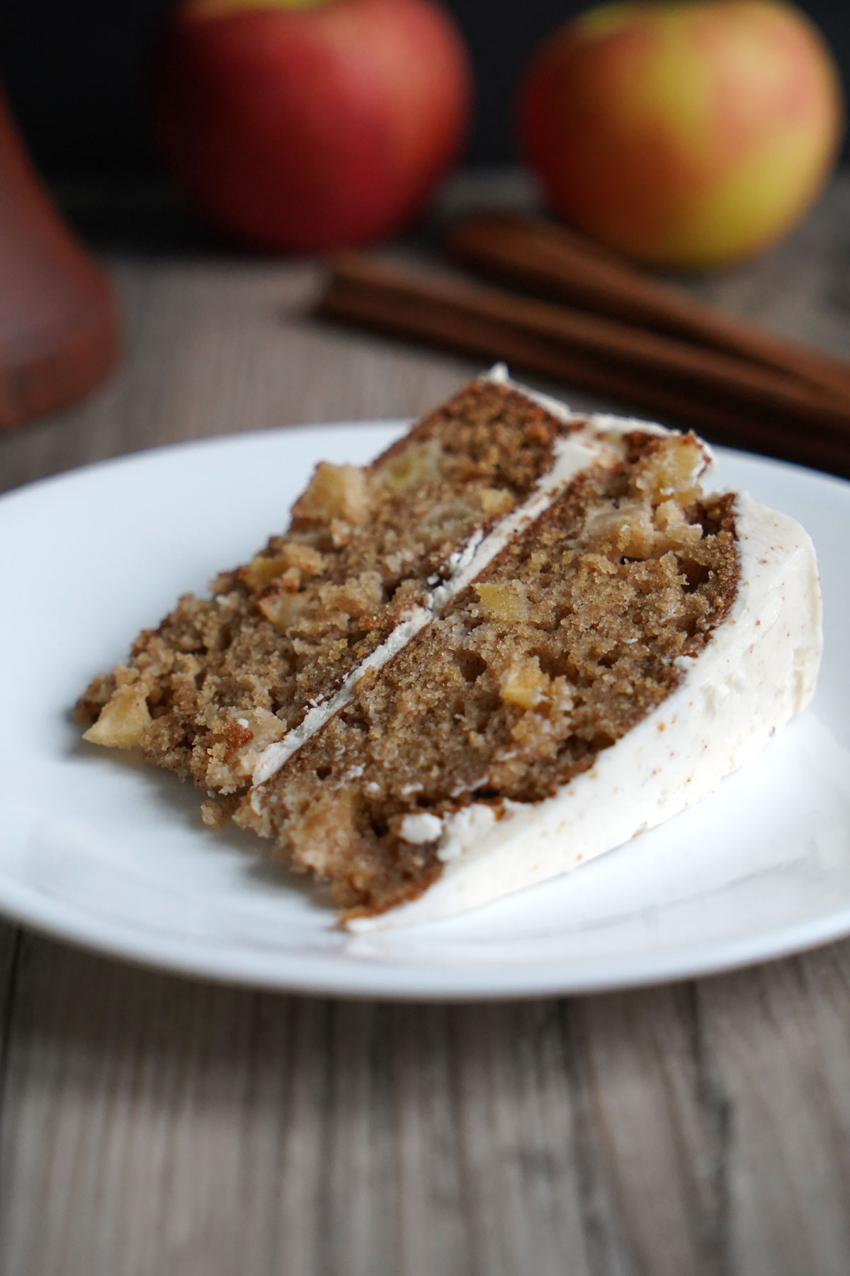 Slice of apple spice cake in a white plate with apples in the backgorund.