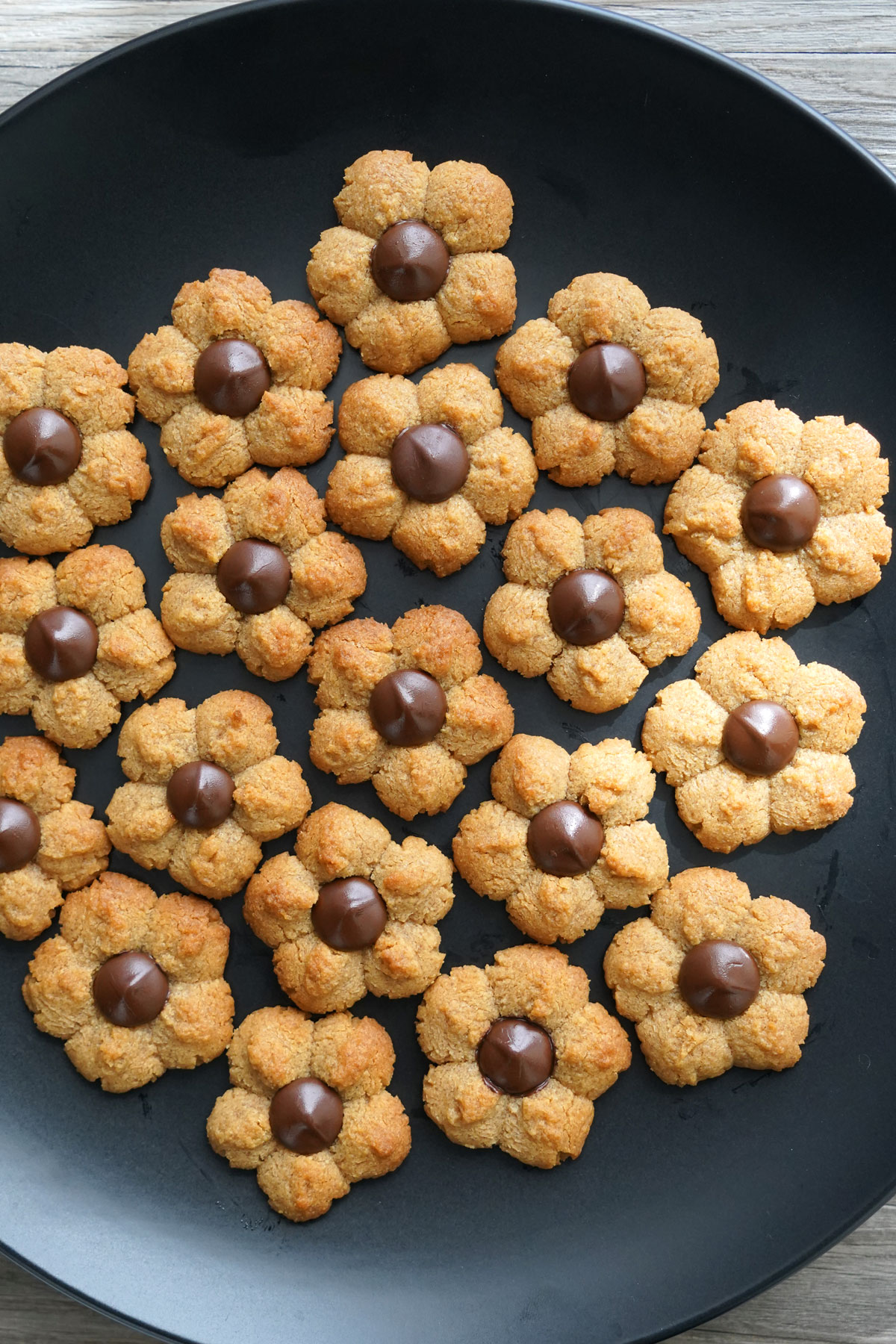 Flower shaped peanut butter blossoms on a black platter.