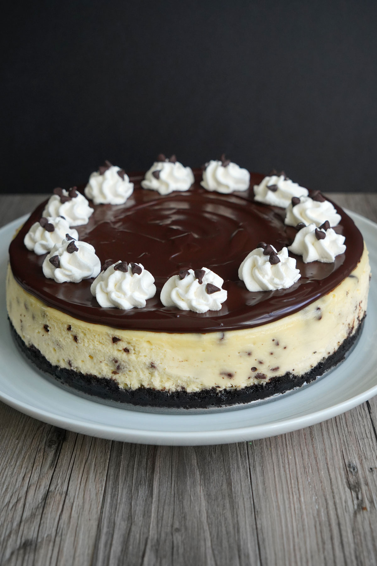 Chocolate Chip Cheesecake with ganache topping and whipped cream decorations on a white platter. 