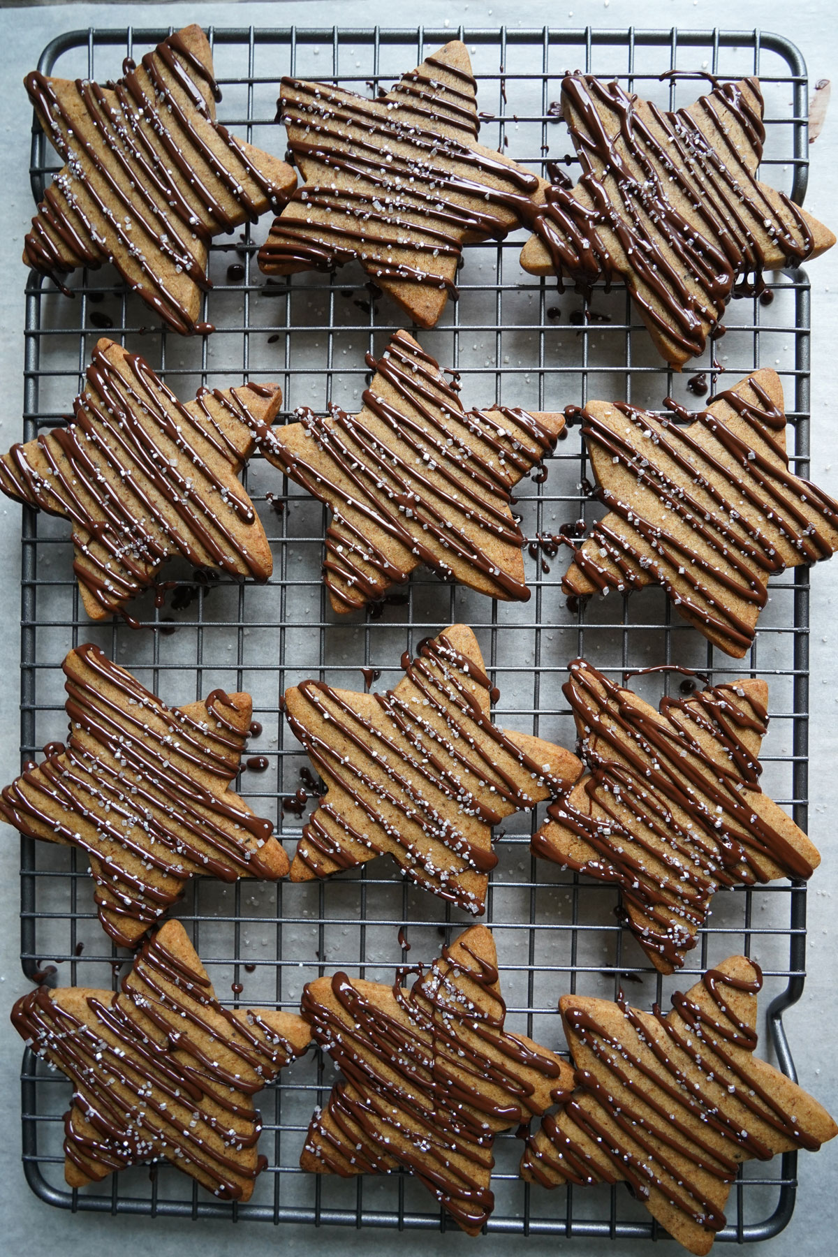 Star shaped sugar cookies with chocolate drizzle, drying on a cooling rack. 